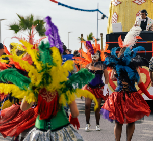 Tänzerinnen in bunten Federkostümen und Masken feiern ausgelassen auf einer Straße beim Karnevalsumzug auf Grenada.