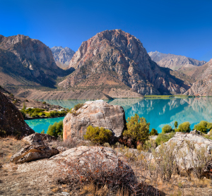 Türkiser Bergsee spiegelt schroffe Gipfel der Fann-Berge, umgeben von Felsen und karger Vegetation.