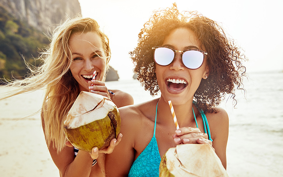 Zwei Frauen mit Kokosnuss in der Hand am Meer genießen Frühbucher Reise