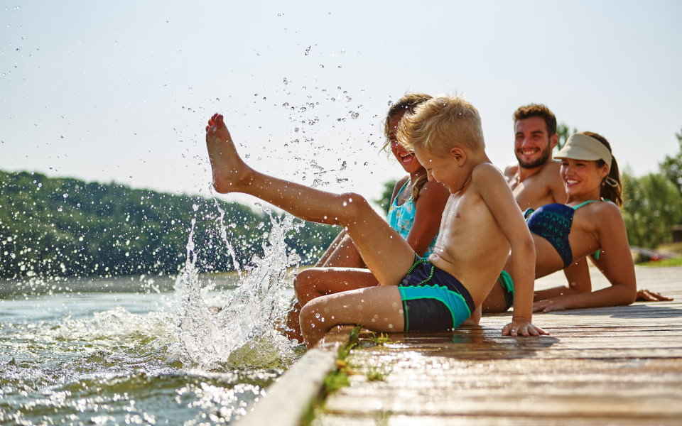 Familie am Gardasee, die am Steg sitzt und mit ihren F&uuml;&szlig;en im Wasser planscht.