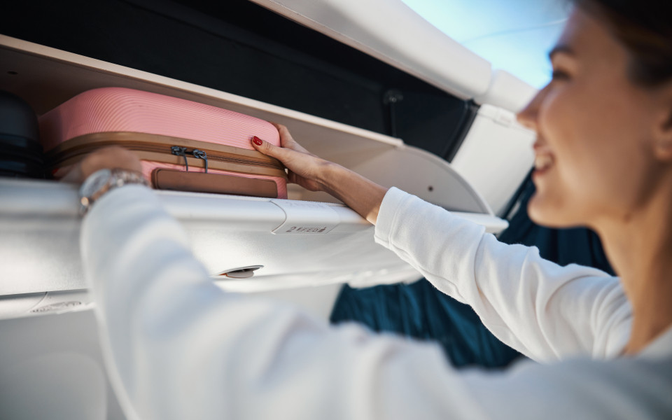 Frau verstaut ihr Handgep&auml;ck im praktischen &Uuml;berkopffach f&uuml;r das Handgep&auml;ck